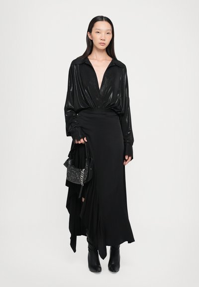 Black long-sleeved blouse with a deep V-neck and shiny texture, paired with a black, flowing skirt. Accessorized with a studded black handbag.