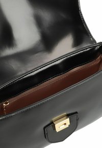 Borsa a mano nera in pelle con finitura lucida, con un interno marrone e chiusura a scatto in tonalità oro. Tasca interna con dettaglio a zip.