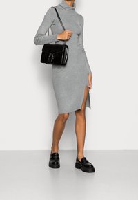 Robe grise à manches longues avec un col montant et une fente sur le côté, assortie à un sac à main noir au motif crocodile et des mocassins épais.