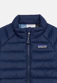 Παιδικό μπουφάν Patagonia σε ναυτικό μπλε χρώμα, με καπιτονέ ύφ ασμα, εμπρόσθιο φερμουάρ και ψηλό γιακά, ετικέτα με μέγεθος 2Τ ορατή στο εσωτερικό του γιακά.