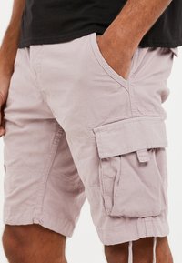 Svetle růžové cargo šortky s texturační látkou, vybavené bočními kapsami a kapsou na stehně s klopou, šitými detaily a šňůrkou na lemu.