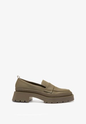 Mocassin en cuir olive, épais, avec une semelle crantée et un petit talon, présentant une sangle cousue à l'avant et une languette au talon.