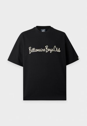 Homme debout, les mains dans les poches, portant un t-shirt noir Billionaire Boys Club, un jean large gris clair et des chaussures noires et blanches.