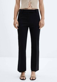 Czarne spodnie typu straight-leg o gładkiej teksturze, z paskiem w talii i prostymi liniami, w połączeniu z beżową prążkowaną bluzką do talii.