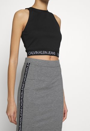 Woman wearing a black crop top with "Calvin Klein Jeans" on the hem and a gray skirt with a vertical "Calvin Klein Jeans" logo strip.