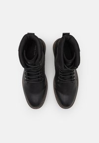 Černé kožené kotníkové boty s texturovaným povrchem, šněrovací design a polstrovaným límcem, s kontrastním prošíváním kolem podrážky.