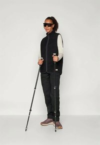 Črna flis jakna z zadrgo na sprednji strani, oblečena čez svetlo dolg rokav. Črne hlače in rjavi planinski čevlji. Dva pohodniška palica.