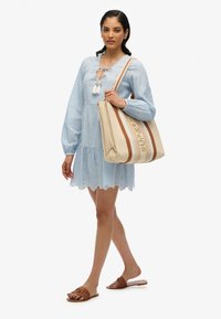 Vestido de tela a rayas de color azul claro, con mangas largas y un dobladillo en forma de onda. Bolsa de mano beige con acentos marrones y el texto "SUPERDRY". Sandalias marrones.