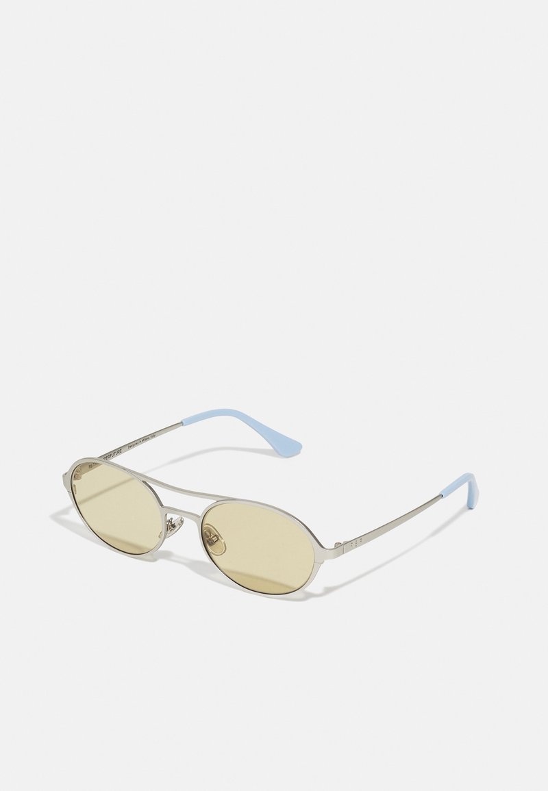 Occhiali da sole ovali con lenti gialle, montatura in metallo argentato e aste in plastica blu. Design minimalista con un logo discreto sul lato.