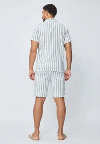 Ensemble de chemise à manches courtes rayée et de shorts en bleu clair avec des rayures blanches et beiges. Fabriqué en tissu respirant ; coupe décontractée.