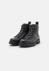 Botas de senderismo de cuero negro con un patrón texturizado, cordones planos, ojales de metal y una suela resistente. Presentan un diseño robusto con asas.