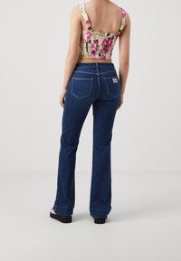 Jeans med hög midja i mörkblå denim med utsvängda ben, som har bakfickor och ett distinkt märke på den högra bakfickan.