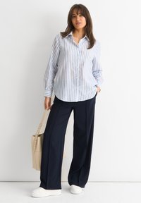 Button-up shirt with blue and white vertical stripes, paired with navy wide-leg pants and white sneakers; carrying a beige tote bag.