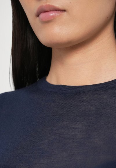 Tumesinine kootud topp, millel on ümmargune kaelus ja peen tekstuur, kärbitud vaade, mis keskendub kraele ja ülemisele kaeluse alale.