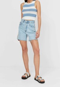 Woman wearing sleeveless blue and white striped knitted crop top, high-waist light blue denim shorts, and silver sandals.