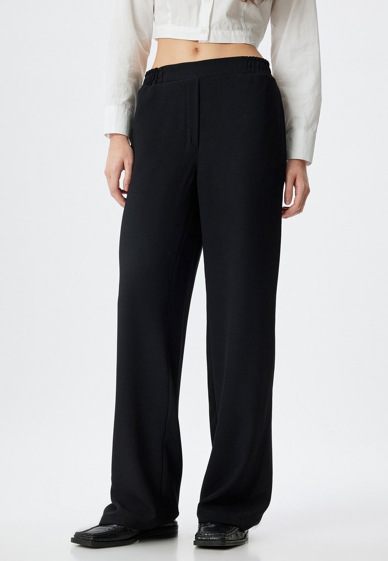 Zwarte wijde broek met een elastische tailleband, gemaakt van een zacht materiaal. Heeft een gladde textuur en een recht, vloeiend ontwerp.
