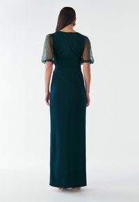 Garšs, pieguļošs kleita tumši zaļā audumā, ar caurspīdīgām pūkām piedurknēm un maziem zilajiem akcentiem, kā arī ar rāvējslēdzēju aizmugurē.