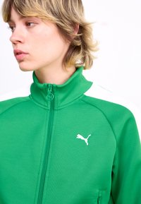 Green zip-up jacket made of textured fabric, featuring white accents on the shoulders and a small white Puma logo on the chest.