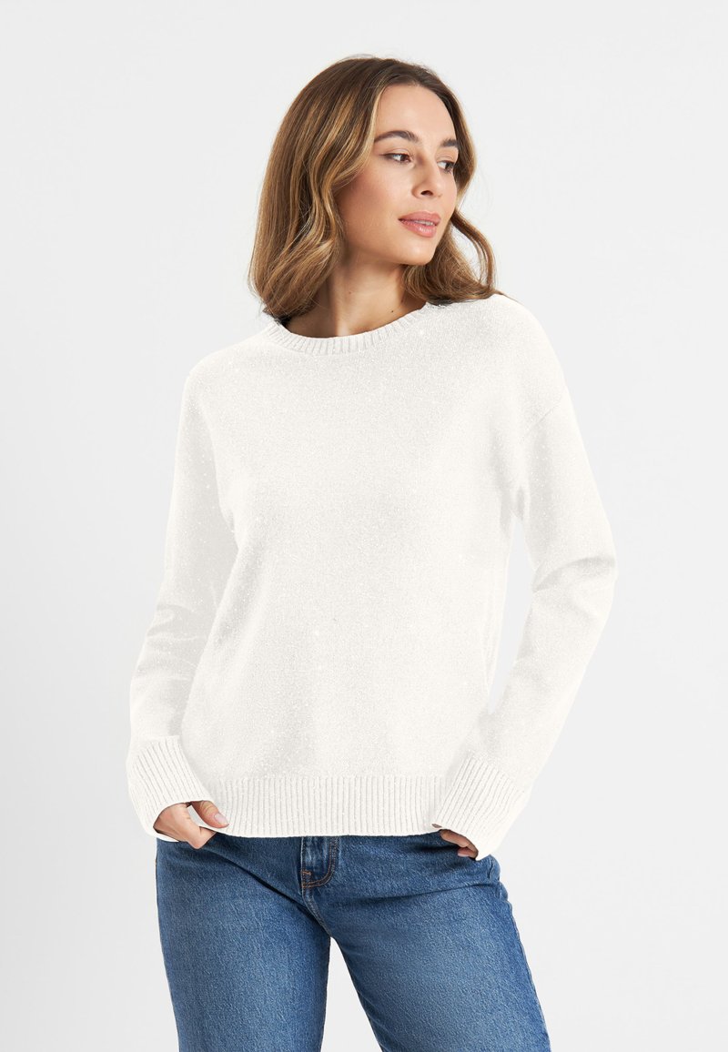 Weißer Strickpullover mit geripptem Kragen und Bündchen. Weiche Textur. Kombiniert mit blauen Jeans, die den lässigen Schnitt betonen.