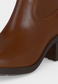 Gros plan d'une bottine en cuir marron avec un bout arrondi et un talon bloc en bois empilé.
