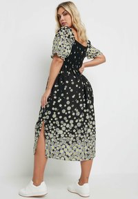 Svart blommig klänning med gula prästkragar, puffärmar, smockad bodice och sidssprund. Matchad med vita sneakers.