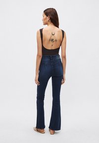 Body negro con la espalda descubierta, vaqueros acampanados de talle alto en azul oscuro y un tatuaje estampado en la espalda con diseños celestiales y de dragón.