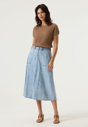 Braunes, geripptes Kurzarmoberteil kombiniert mit einem hellblauen Jeans-Maxirock mit Knöpfen vorne und Seitentaschen, getragen mit braunen Sandalen mit Blockabsatz.