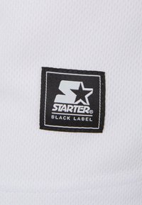 Tela blanca con una etiqueta cuadrada negra que dice "STARTER" y una estrella, junto con "BLACK LABEL" en una fuente más pequeña debajo.