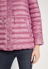 Puffig, mid-lång jacka i ljusrosa med en vadderad design. Har sidofickor, dold dragkedja och dragsko för justeringar.