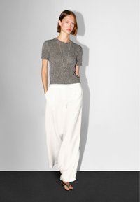 Szary, dziergany top z krótkim rękawem zestawiony z białymi, luźnymi spodniami. Długi srebrny naszyjnik jako akcent. Minimalistyczne tło.