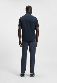 Marineblaues ärmelloses Oberteil mit hohem Kragen, kombiniert mit dunklen Hosen und Sportschuhen, bietet eine glatte Textur und minimalistisches Design.
