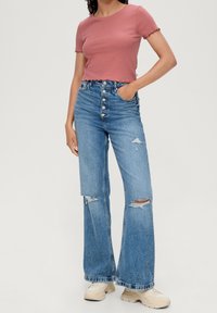 Lyserød cropped t-shirt med bølgede kanter, parret med høj talje og bred ben blå jeans med slidte detaljer og knaplukning.