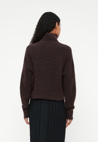 Burgundy stickad tröja med hög krage, avslappnad passform och långa ärmar. Mjuk textur, kort längd, matchad med en texturerad svart kjol.