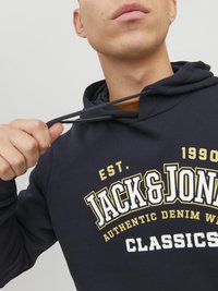 Felpa blu navy con cappuccio e lacci, caratterizzata da un design grafico testuale in bianco e oro "JACK & JONES CLASSICS" sulla parte anteriore.