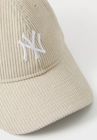 Beige kord szövet sapka ívelt karimával, a frontján fehér kiemelt 'NY' logóval. Texturált anyag látható bordázattal.