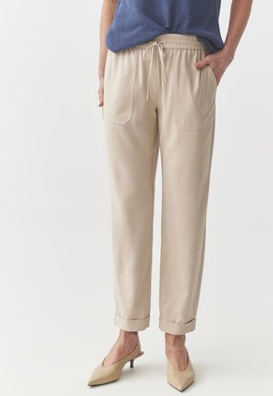 Beige elastické kalhoty v pase na šnůrku s dvěma předními kapsami a ohrnutými manžetami, kombinované se modrým pleteným topem a béžovými botami.