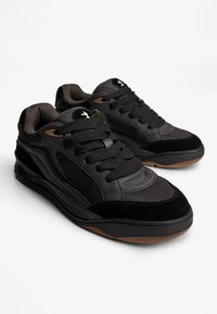 Adidași negri, cu un amestec de material sintetic neted și plasă texturată. Talpa din cauciuc, șireturi rotunde și un accent subtil cu logo.