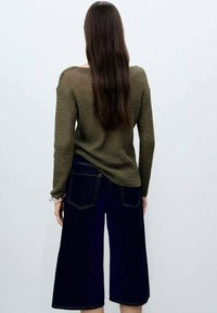 Maglione lavorato a maglia verde oliva con maniche lunghe e vestibilità ampia, abbinato a jeans cropped a gamba larga blu scuro con tasche posteriori.