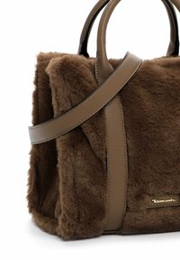 Sac fourre-tout en fausse fourrure marron avec des poignées en cuir lisse, forme structurée et détail de logo doré. Texture douce avec une construction solide.
