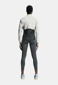 Chaqueta corta ligera en gris con una sección inferior negra. Cuenta con mangas largas y un diseño minimalista. Combinada con leggings grises.