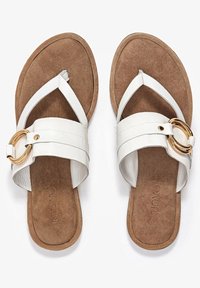 Bílé sandály s jedním širokým páskem zdobeným zlatým kruhovým detailem, měkkou semišovou stélkou a plochou podrážkou pro pohodlí.