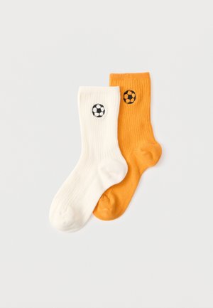 Paire de chaussettes côtelées, une blanche et une orange, chacune arborant un petit ballon de football noir et blanc brodé près du haut.