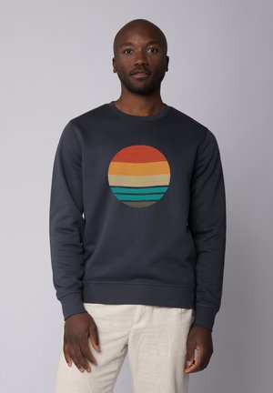 Navy sweatshirt featuring a circular graphic with horizontal stripes in orange, yellow, beige, and teal. Ribbed cuffs and neckline.