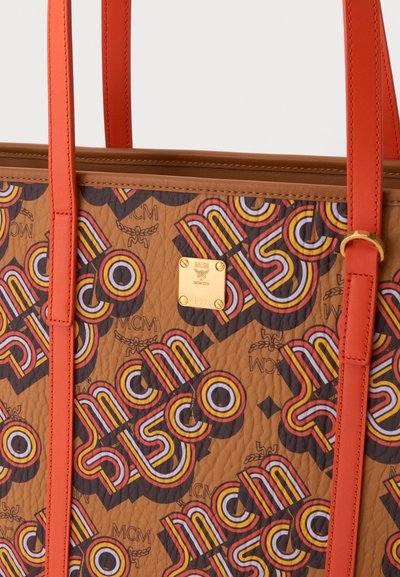 Sac cabas MCM beige et marron avec un motif coloré répétitif du logo et des anses en cuir orange avec détail de boucle dorée.