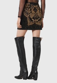 Czarna mini spódnica z misternym haftem z złotych koralików w kwiatowe wzory. Połączona z czarnymi skórzanymi botkami za kolano. Teksturowane wykończenie.