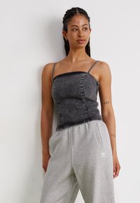 Crop top en denim noir avec des bretelles fines, un col droit et de subtils accents pailletés. Associé à un pantalon de survêtement gris clair avec des poches latérales.