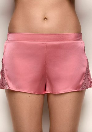 Mujer con shorts de satén rosa con borde de encaje en los laterales, desde la cintura hasta la mitad del muslo, visibles contra un fondo liso.
