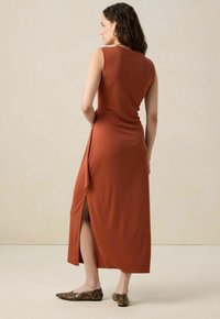 Robe maxi sans manches couleur rouille avec fente sur le côté, silhouette ajustée et texture lisse. Assortie à des ballerines à imprimé serpent.