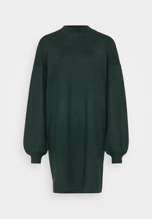 Dunkelgrünes, übergroßes Strickkleid mit hohem Kragen, fallenden Schultern und voluminösen langen Ärmeln. Weiche Textur mit glatter Oberfläche.