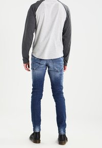 Gray and dark gray long-sleeve shirt with raglan sleeves, paired with blue slim-fit jeans and black shoes, viewed from the back.